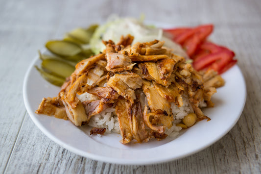 Plate of shredded chicken over rice with pickles and tomatoes on a wooden surface