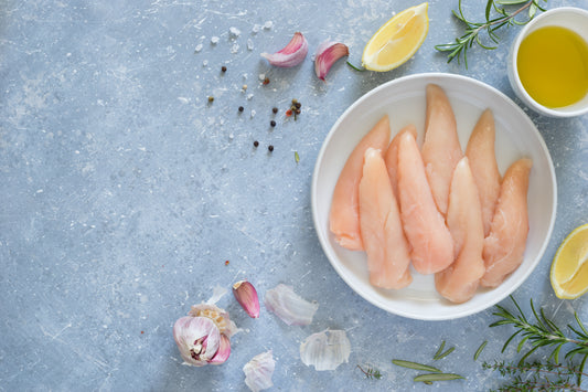 Raw chicken fillets in a bowl with lemon, rosemary, and oil on a blue surface